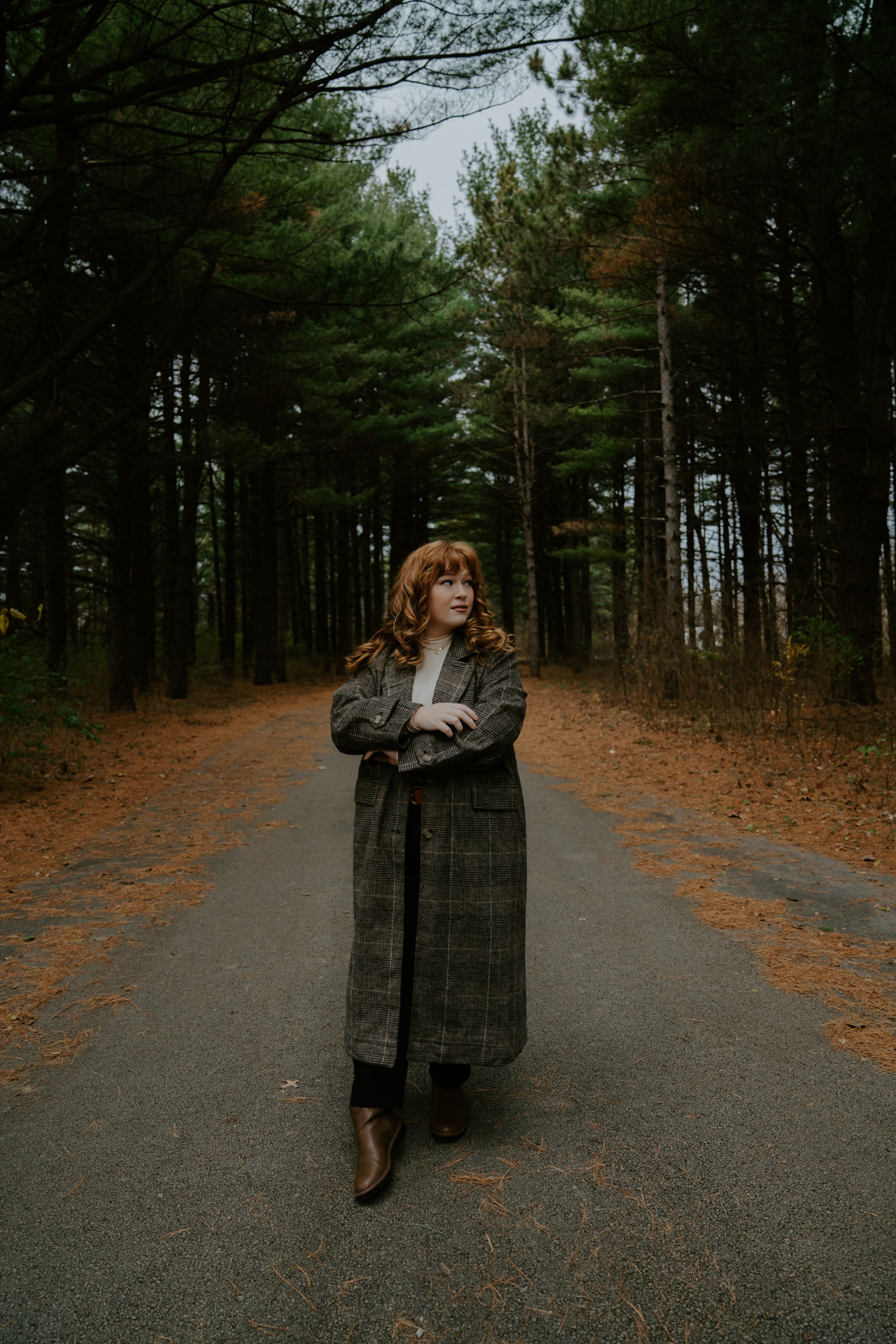 Person in winter coat standing on a winding path through an evergreen forest.