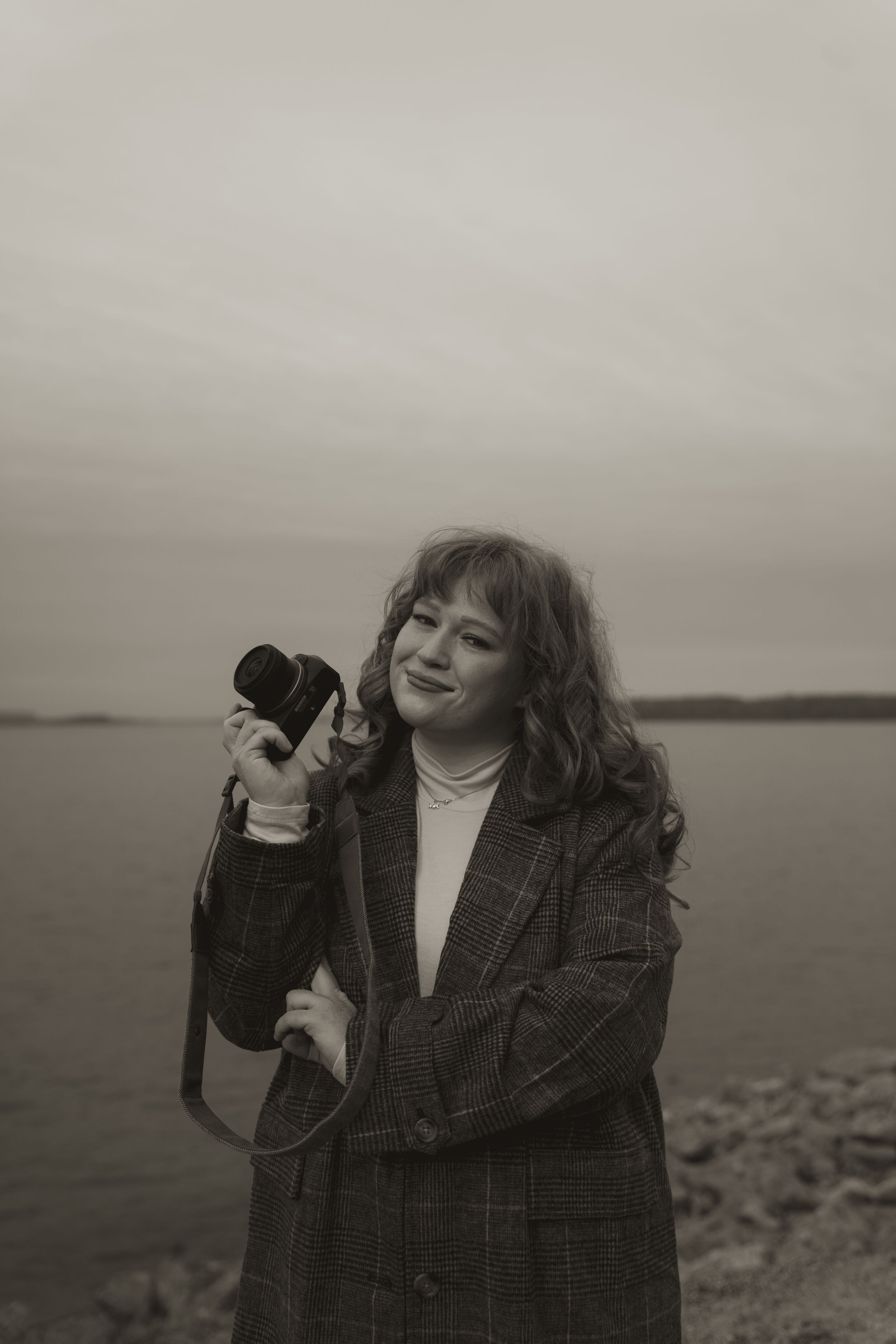Moody black and white portrait with vintage phone against cloudy coastal backdrop.