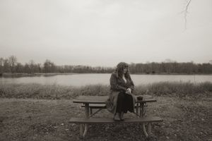 Wide landscape view of figure on picnic bench by serene lakeside.