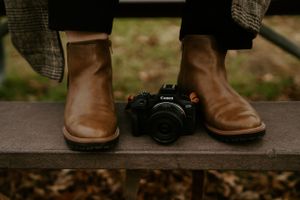 Still life of brown leather boots and camera on wooden surface.