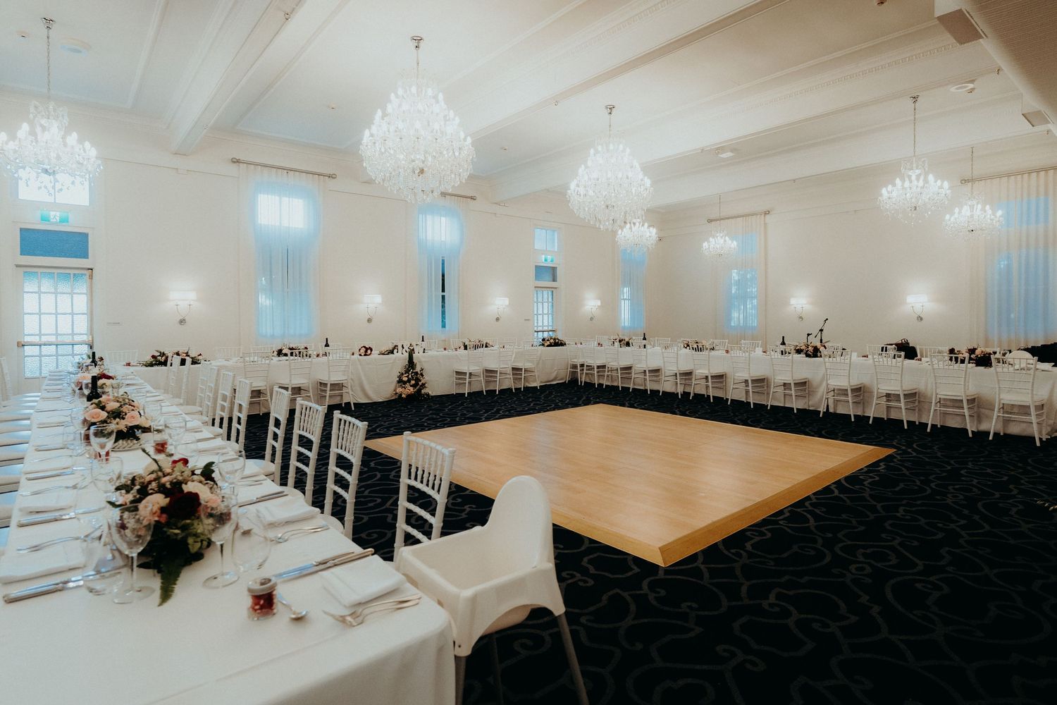 Elegant wedding reception ballroom with crystal chandeliers, dark carpeting, and white tables set for formal dining.