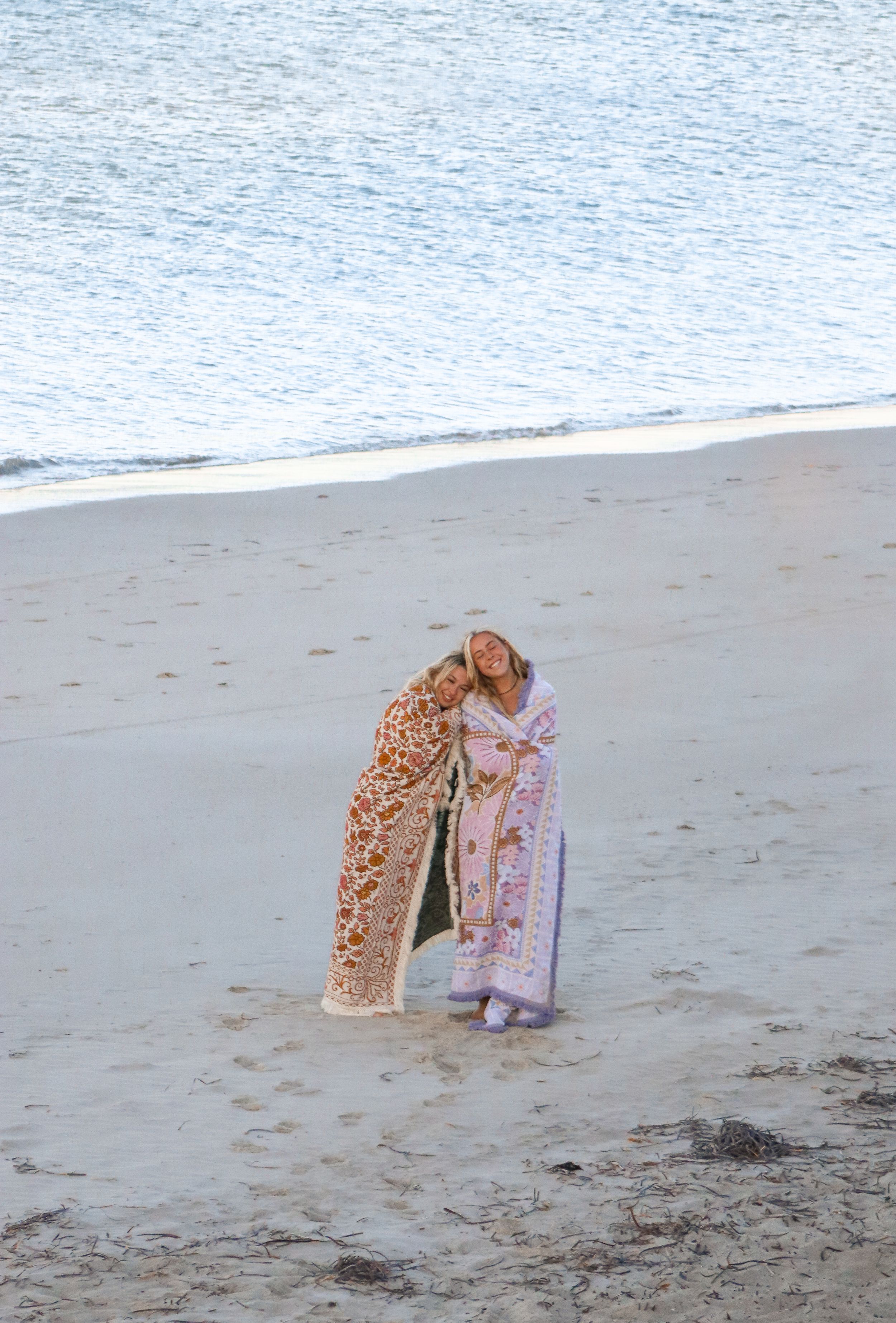 Two friends share an intimate moment on the beach while wearing decorative patterned coverups.