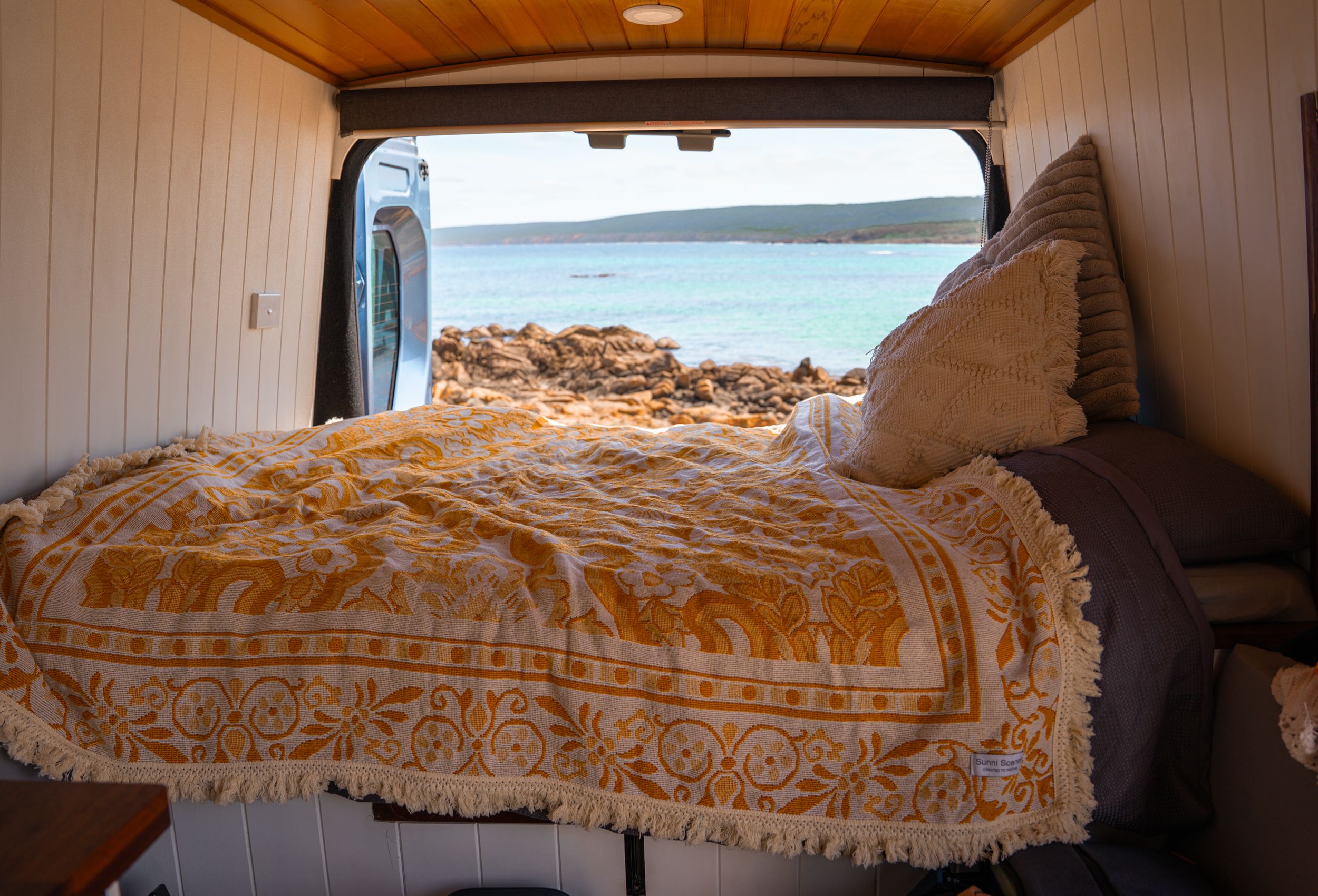 Interior view of van conversion with yellow floral bedding and ocean vista.