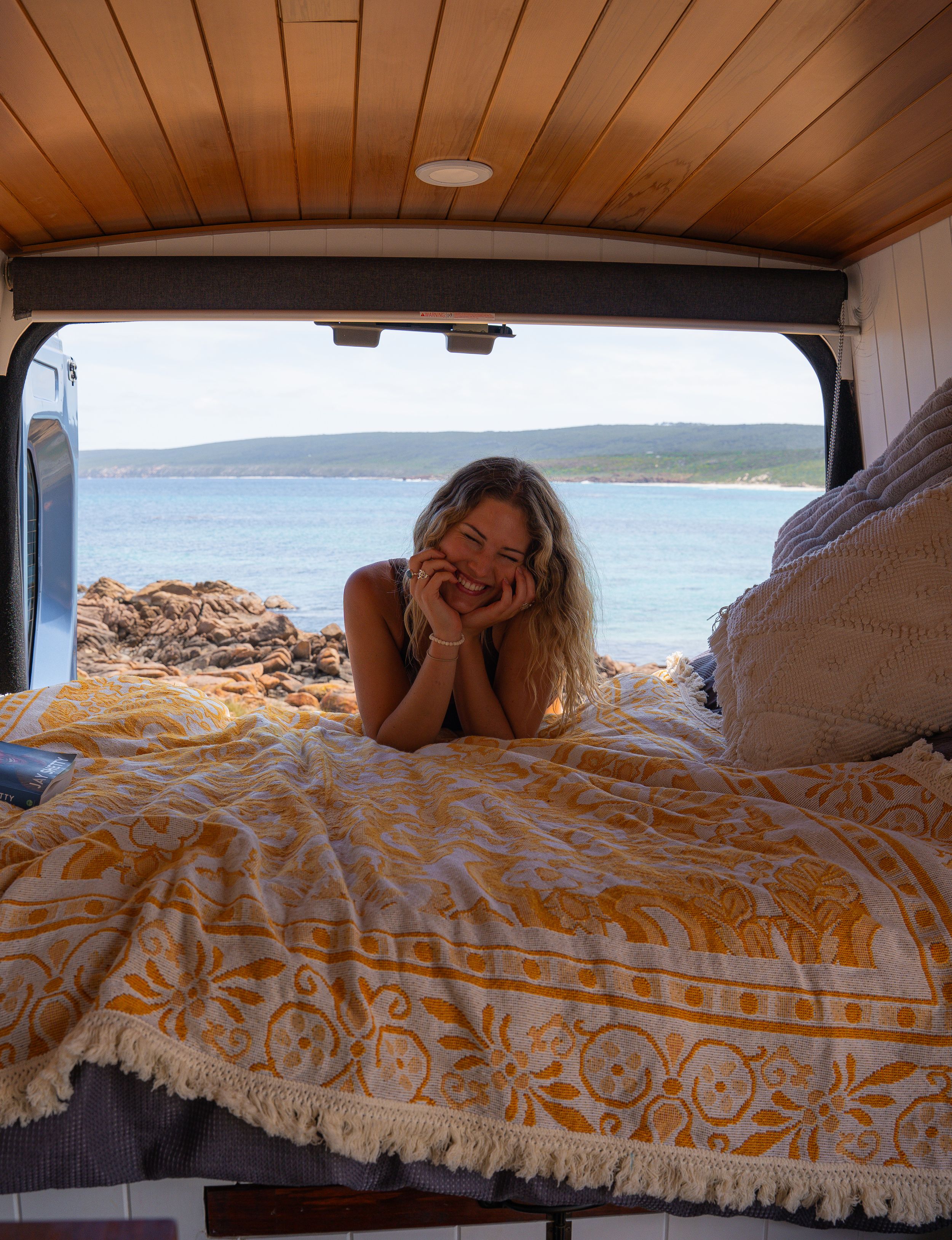 Cozy camper van interior with yellow patterned bedding overlooking coastal view.