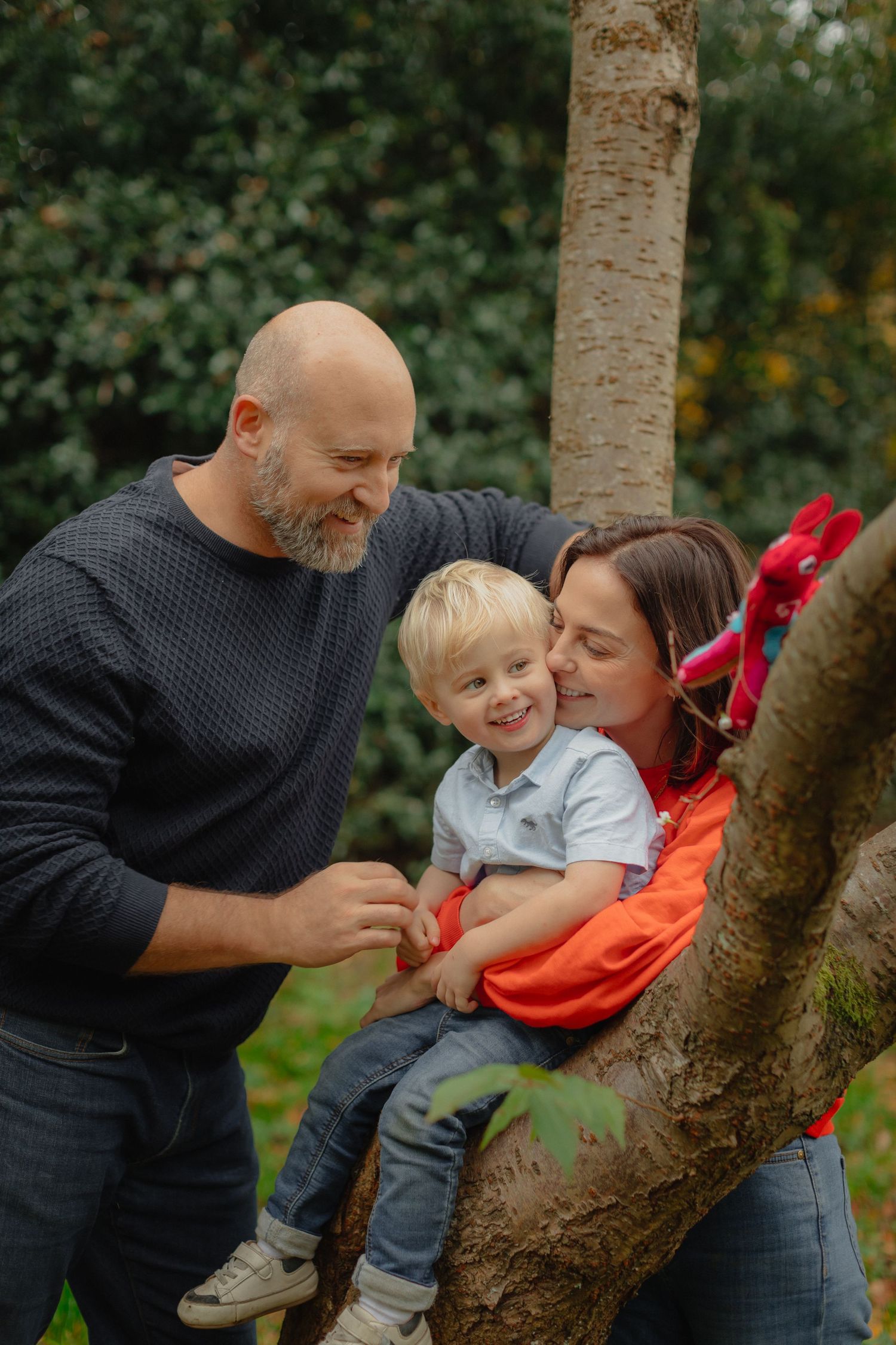 A family shares joyful moments while playing together near a tree trunk in a garden setting.