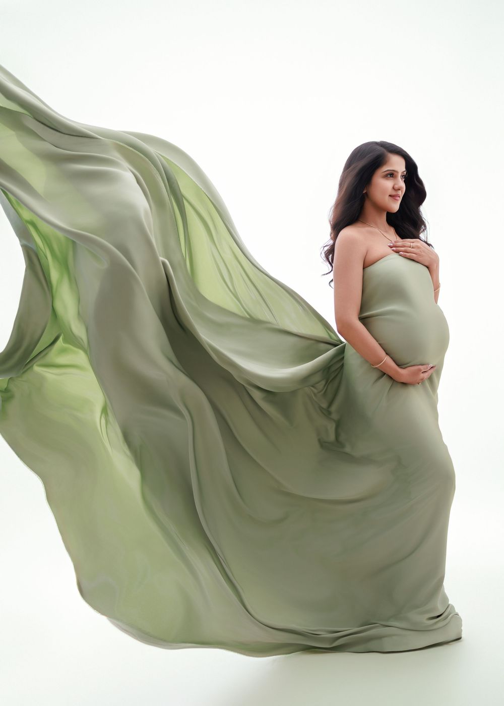 Flowing sage green maternity gown creates ethereal movement in sequence of elegant poses against white backdrop.