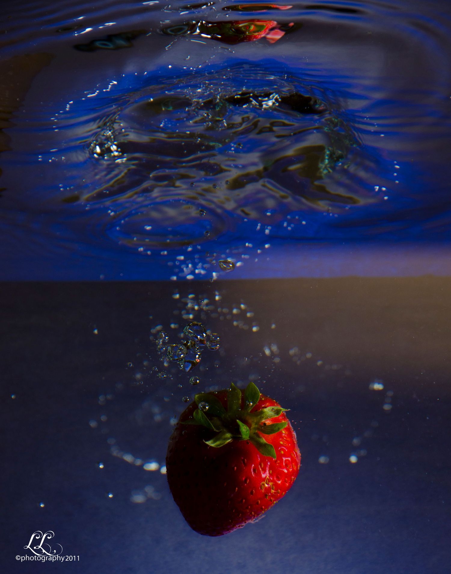 A sequence of strawberries splashing into blue water was captured in high-speed photography with dramatic lighting.