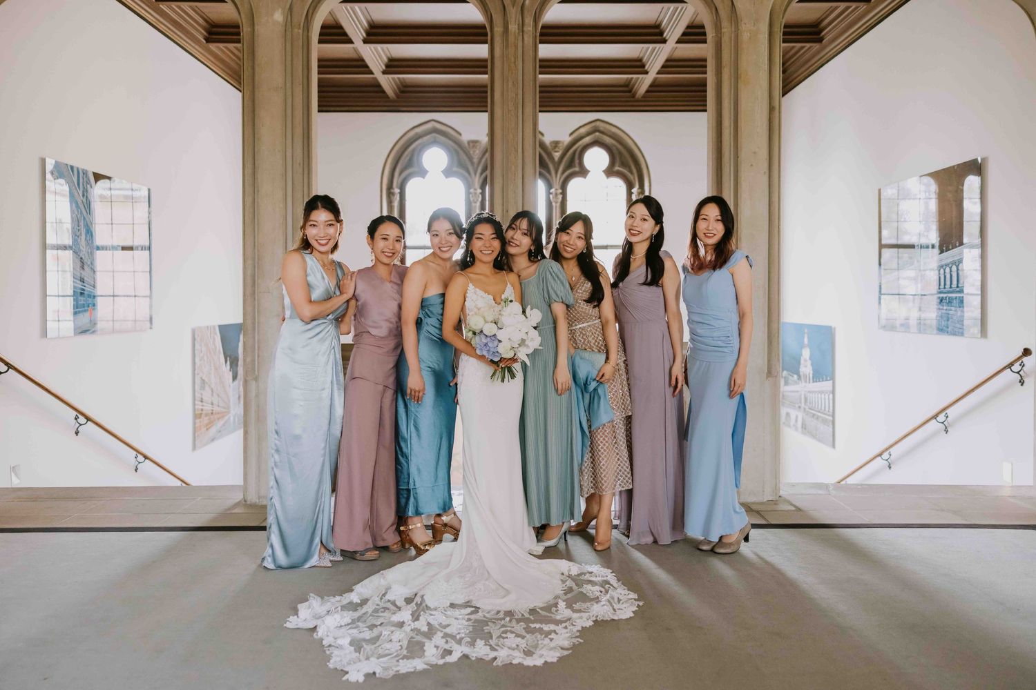 Bridesmaids wearing different shades of blue and neutral colored dresses pose together in an elegant hallway setting.