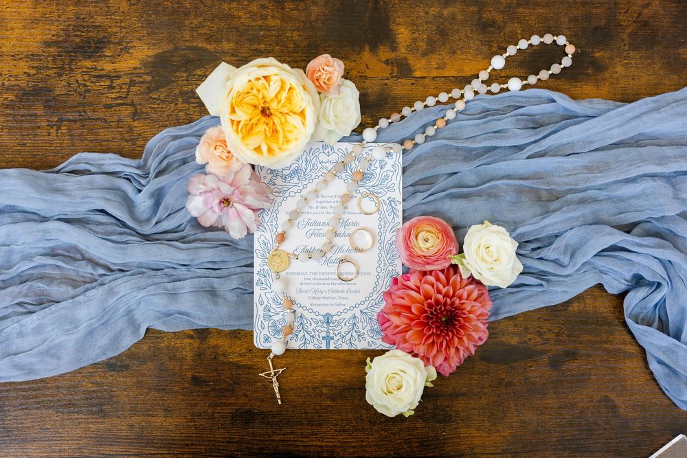 Wedding details featuring a light blue fabric, floral decorations, and ornate paper elements on a rustic wooden surface.