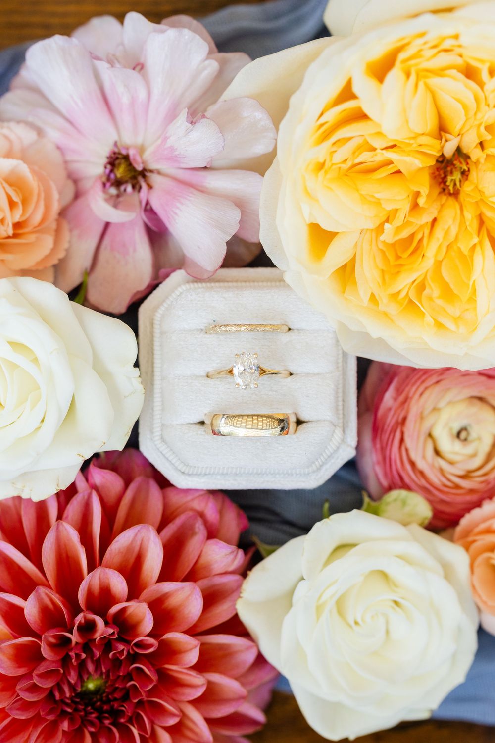 Wedding rings nestled in a white box surrounded by colorful roses, dahlias and ranunculus flowers.