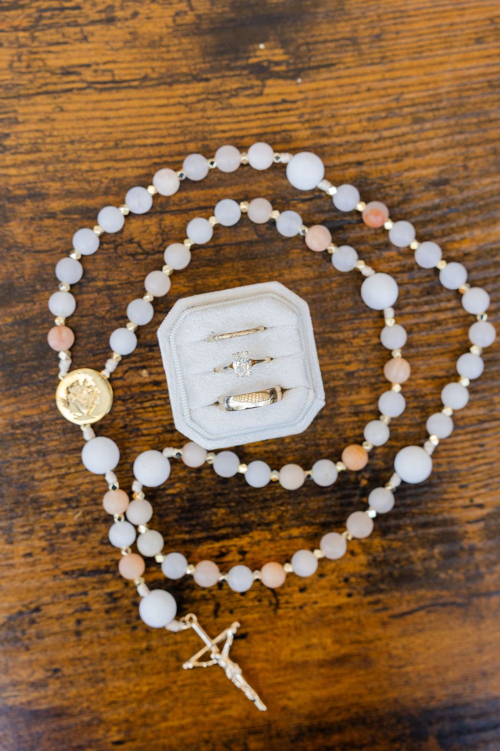 A gold and pearl rosary necklace laid out in different arrangements on a rustic wooden surface shows intricate details.