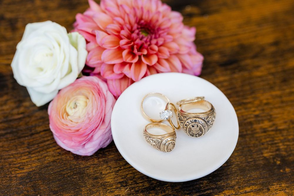 Elegant engagement rings displayed on small white plates with pink and white flowers on a wooden surface.