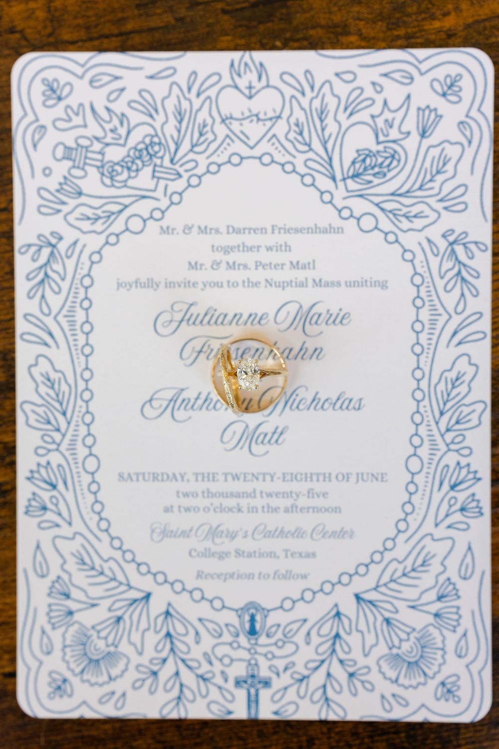 Elegant wedding invitation with ornate blue floral border design and gold text on white paper.