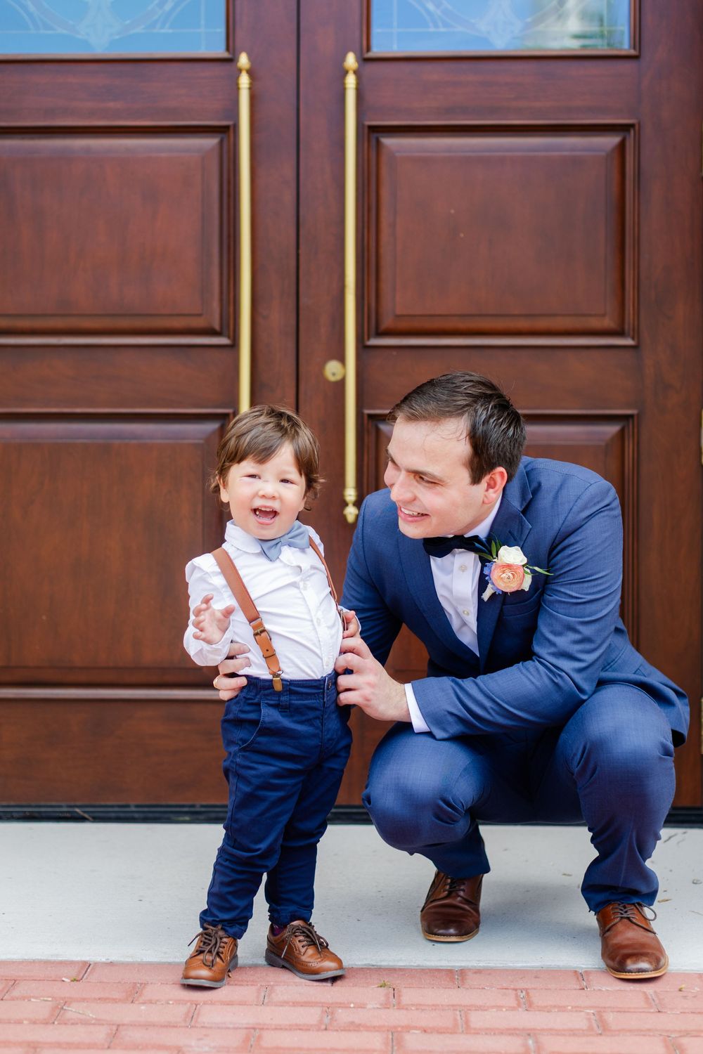 Two people in coordinating navy and white outfits stand in front of large wooden doors at a formal event.