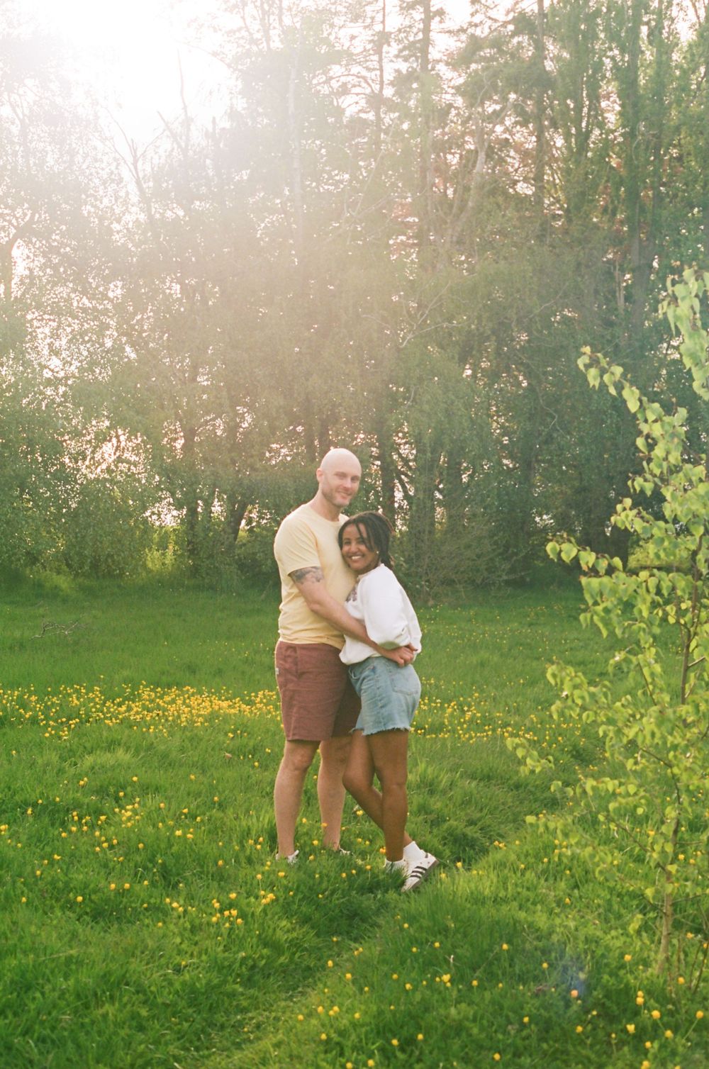 Couple embracing in a sun-drenched field with yellow wildflowers.