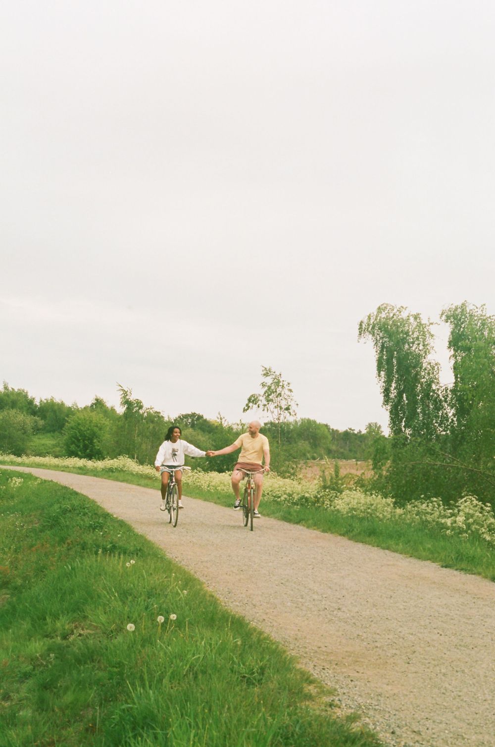 Two cyclists riding along a winding dirt path through green countryside.