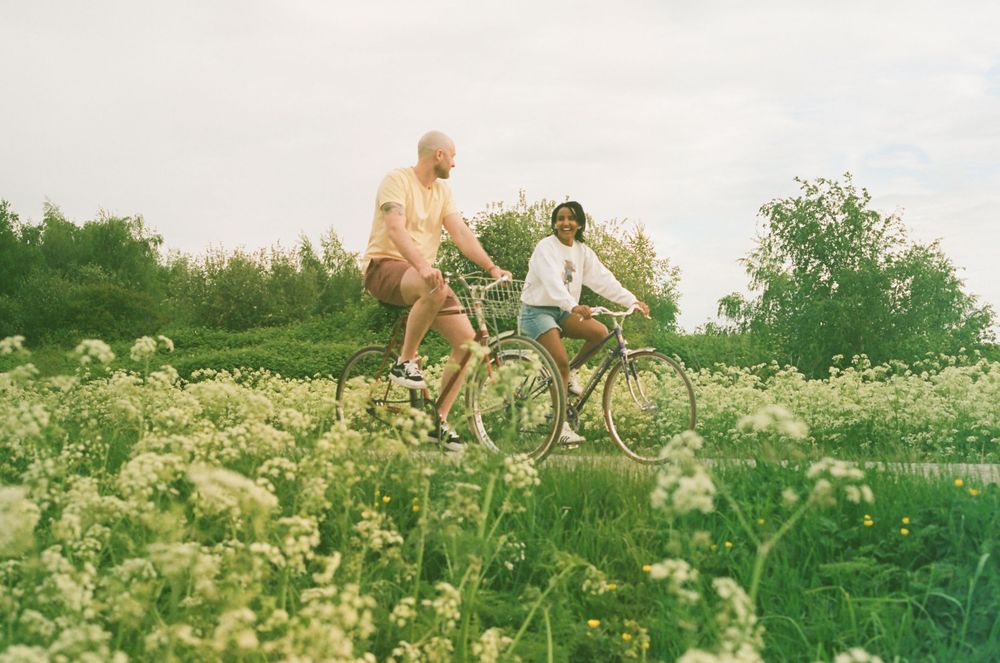 Cyclists riding vintage bicycles through a scenic countryside path on a cloudy day.