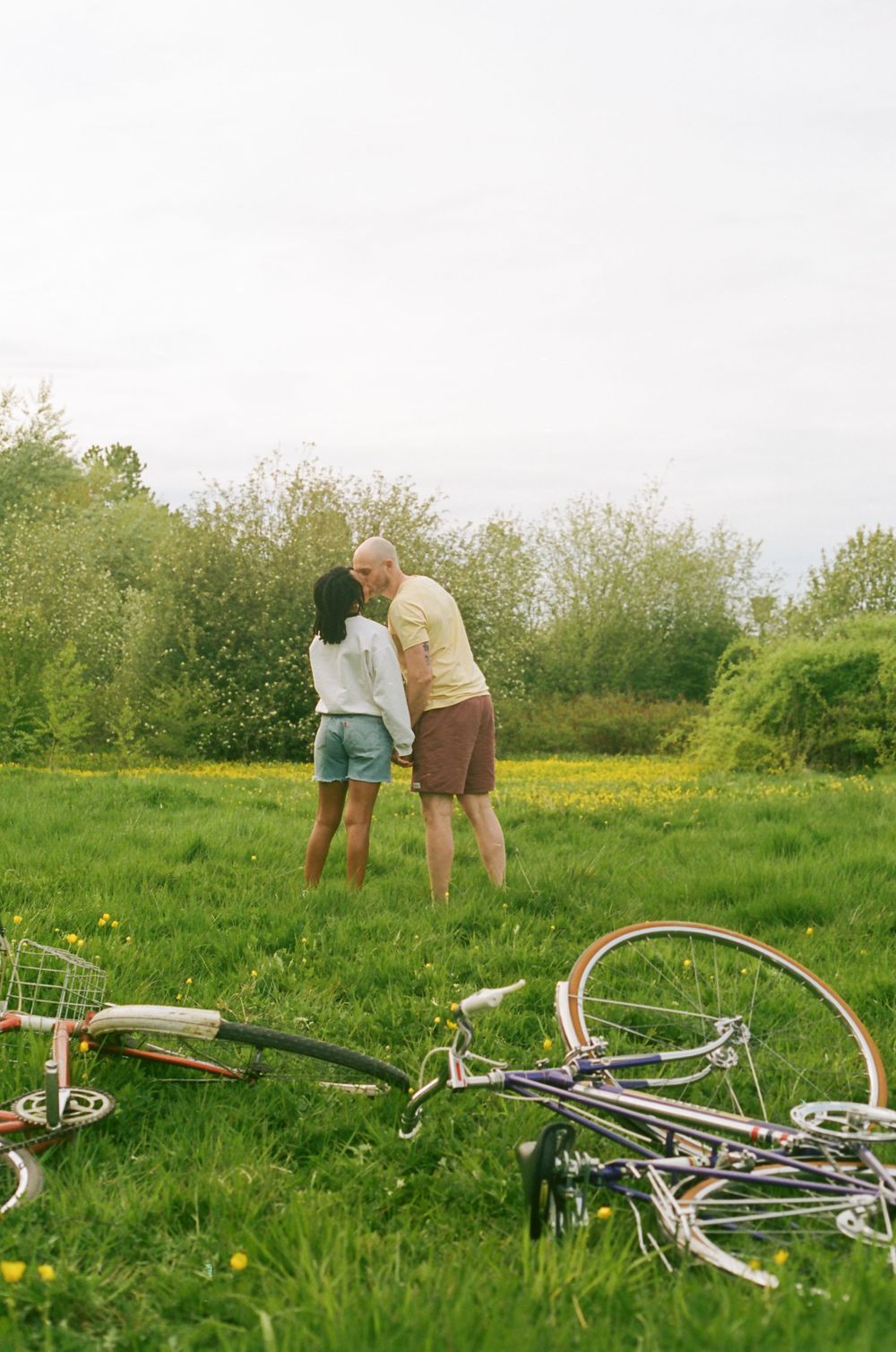 Two people standing in a field with abandoned bicycles lying in the grass.