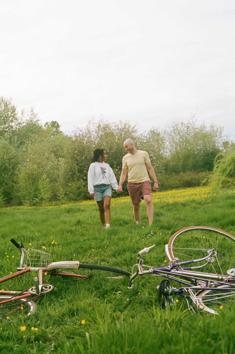 People walking away from discarded bicycles in a sunlit meadow filled with wildflowers.