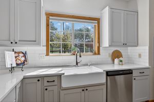 Modern kitchen with gray cabinets, farmhouse sink, white subway tile backsplash, and a bright window overlooking greenery.