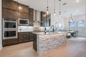Modern kitchen with dark wood cabinets, stone island, stainless steel appliances, pendant lights, and open dining area.