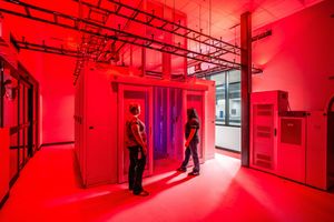 Two people standing in a vibrant red-lit data center server room with industrial ceiling pipes.