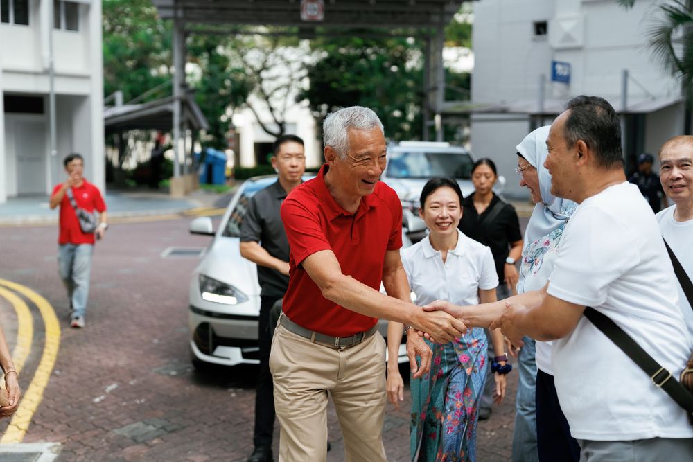 People greet each other warmly on a street corner with handshakes while others look on in an urban setting.