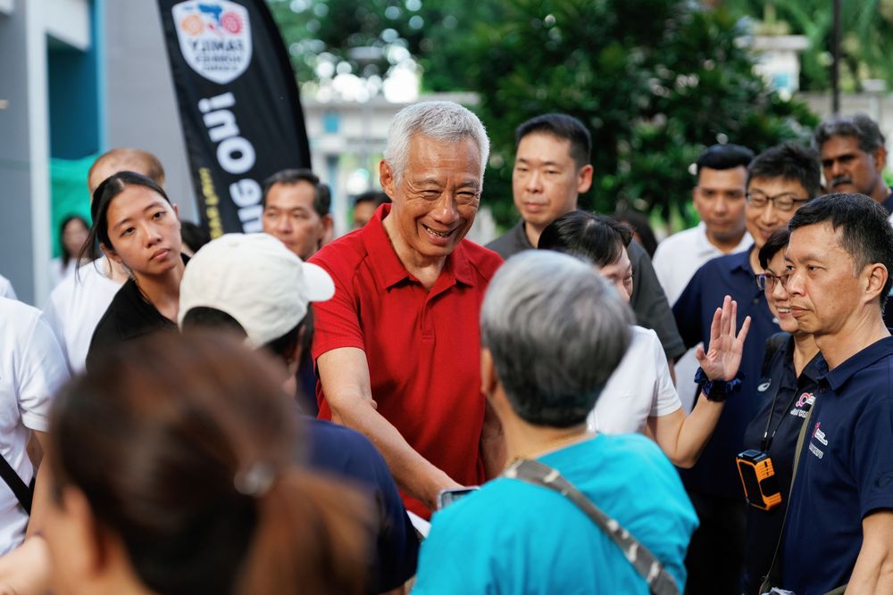 A crowd of people gathered on a Singapore street with someone in a red polo shirt addressing others.