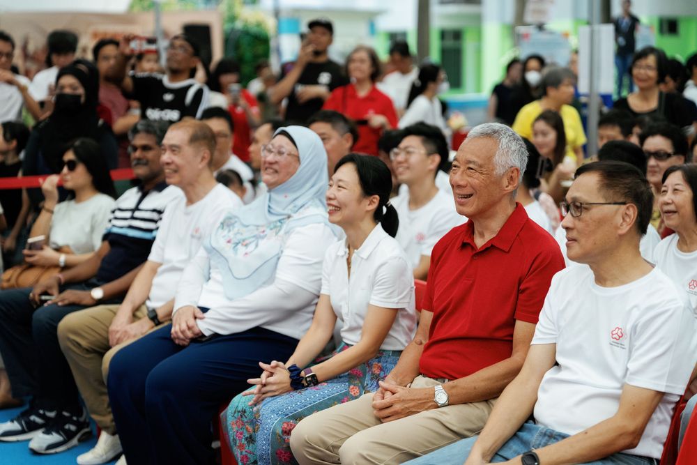 A group of people sitting in rows and watching while smiling and showing positive expressions at an indoor event.