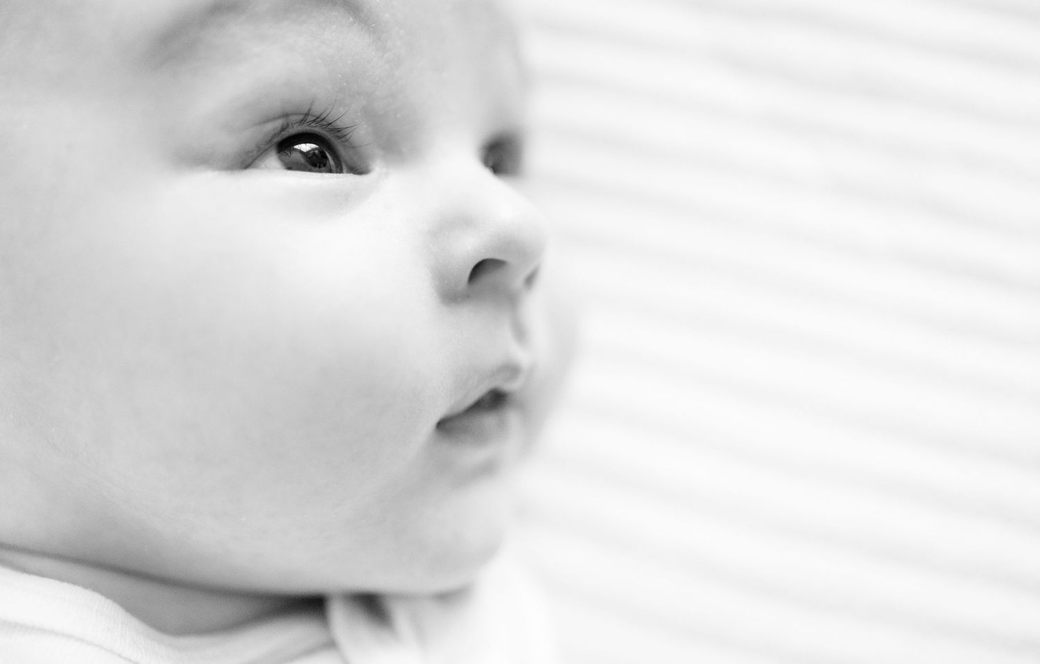A black and white close-up view of an infant's face looking off to the side with soft lighting and dreamy expression.