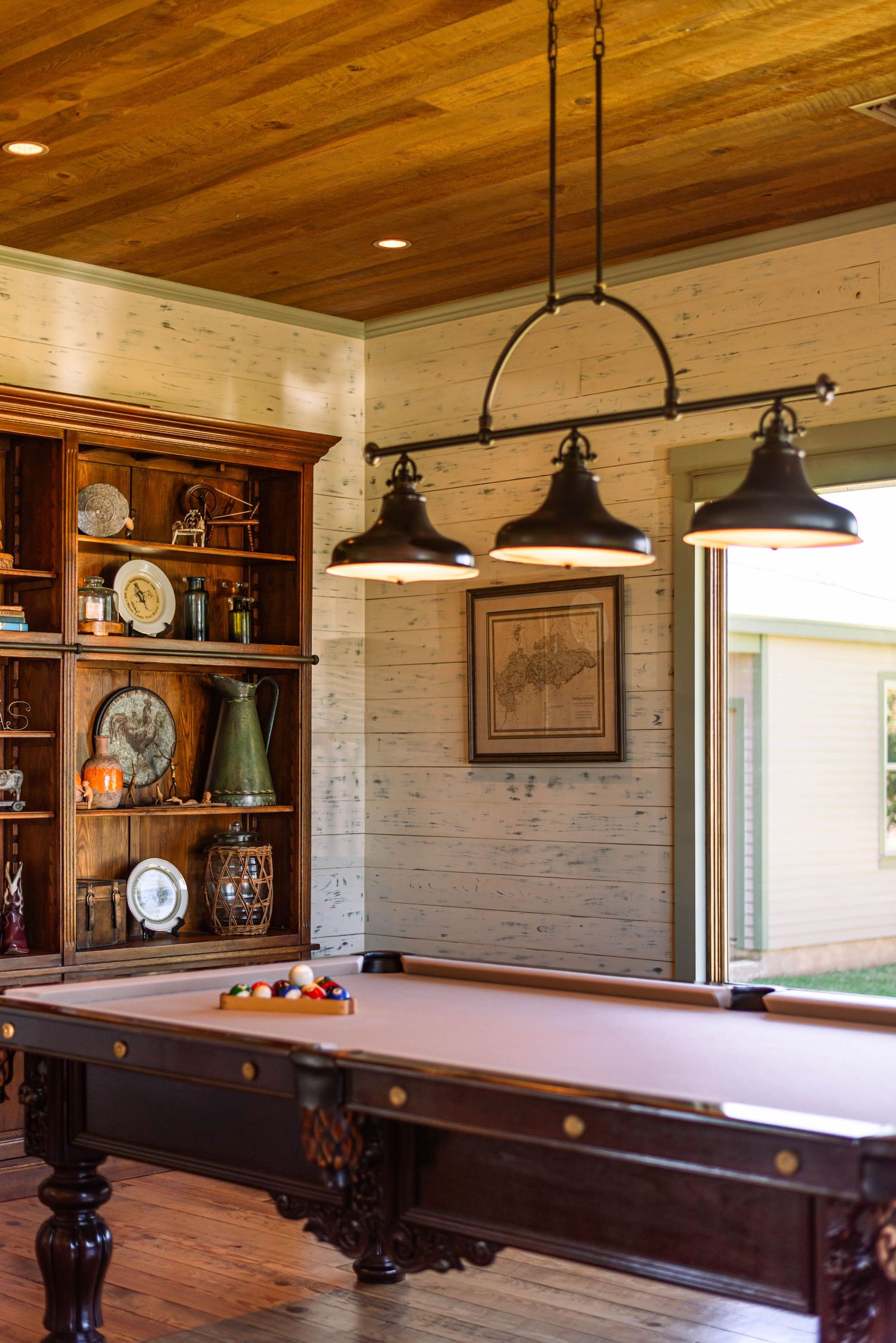 Game room with wooden ceiling, pendant lights, and multiple pool tables in rustic setting.