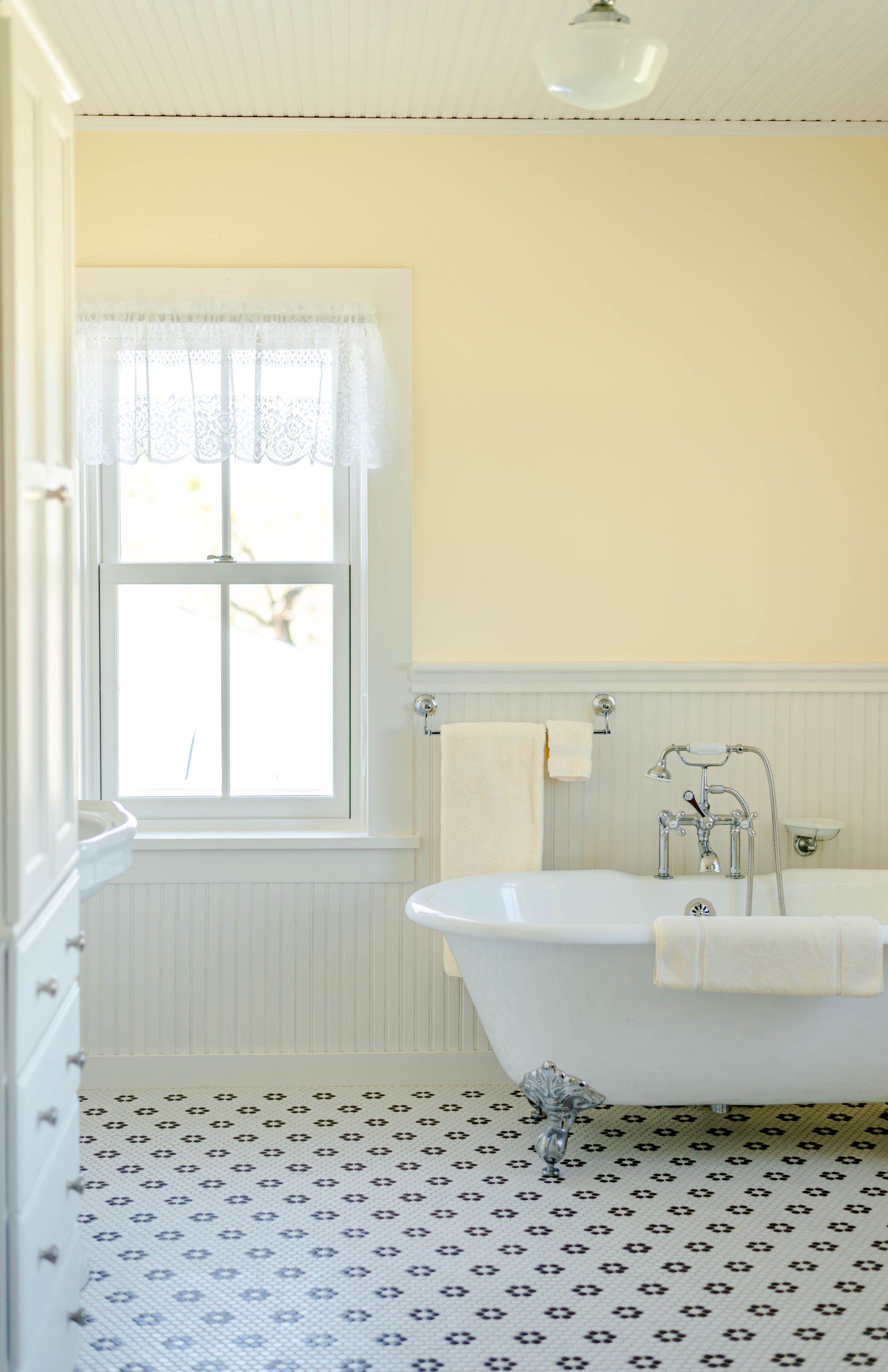 Elegant vintage bathroom with white wainscoting, clawfoot tub, and geometric tile flooring in black and white pattern.