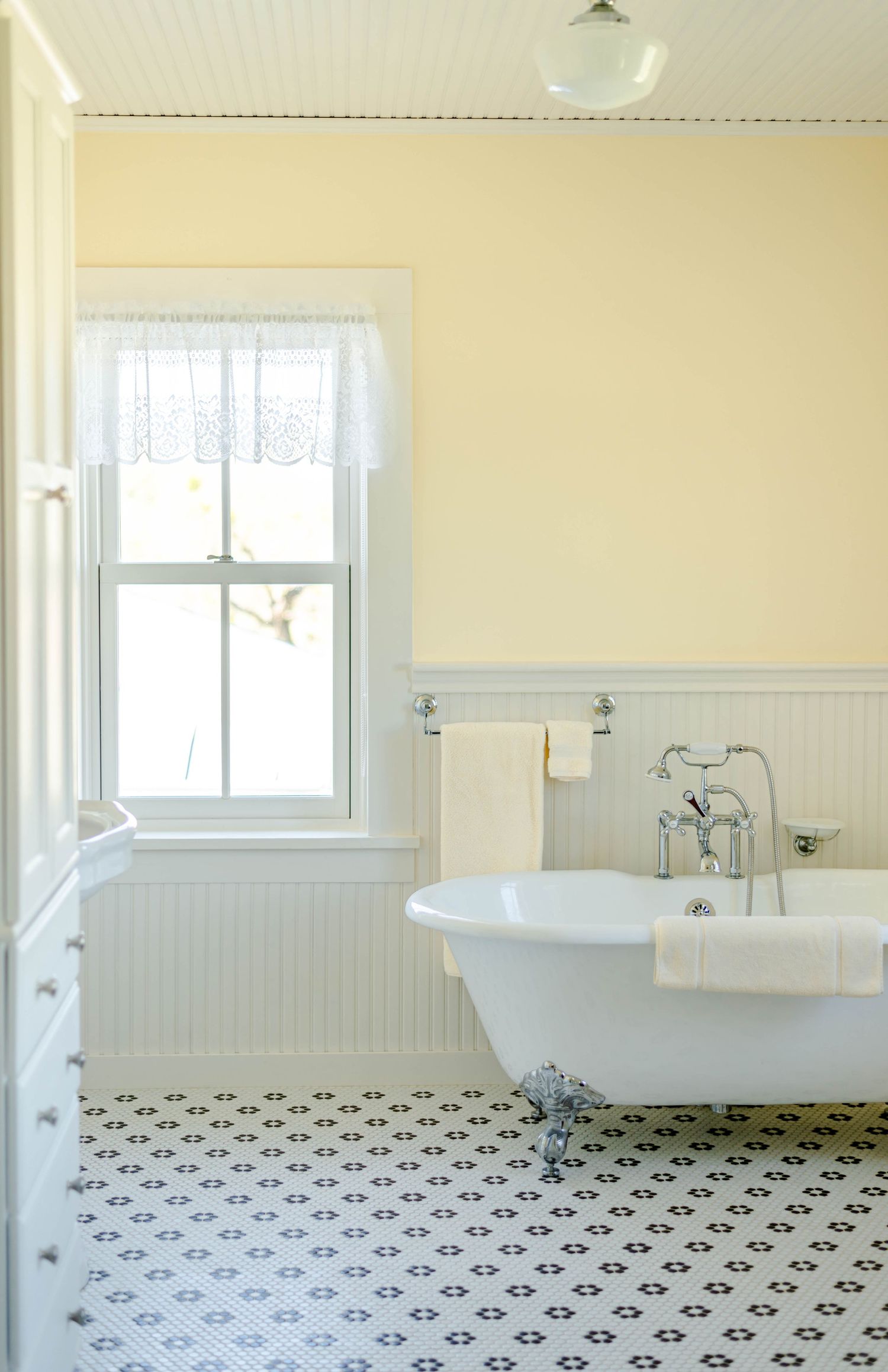 Elegant vintage bathroom with white wainscoting, clawfoot tub, and geometric tile flooring in black and white pattern.