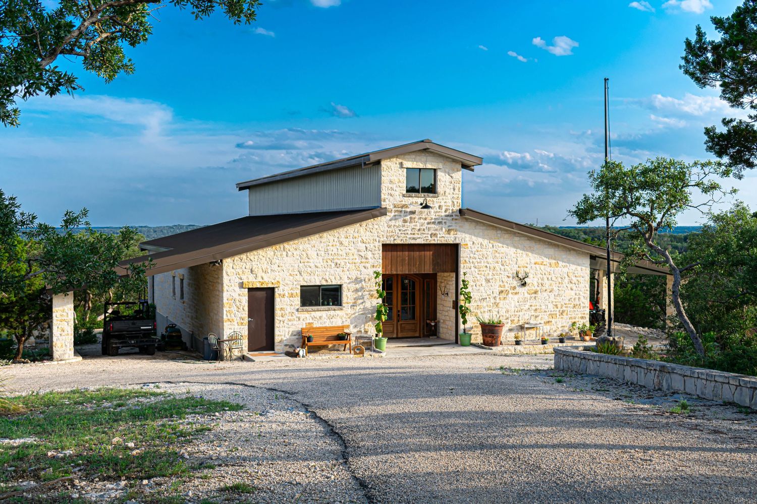 Panoramic view of a stone building exterior with gravel driveway under bright blue sky.