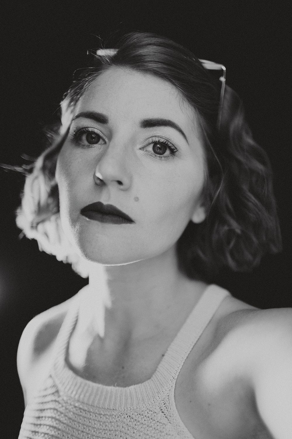 Black and white portrait featuring vintage-inspired makeup and soft curled hairstyle against dark background.