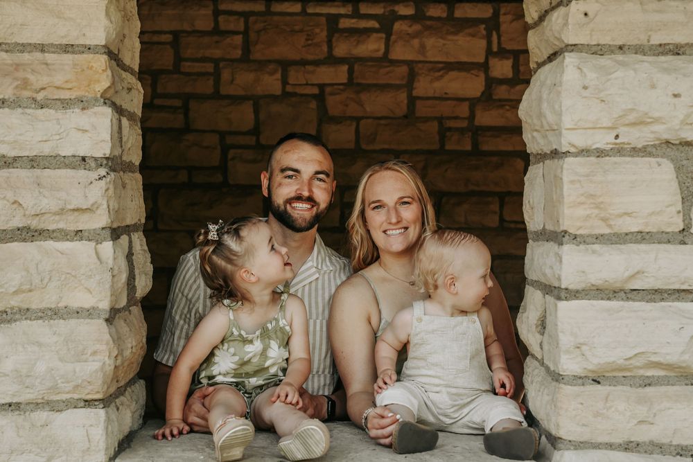 Couple sits together in rustic stone archway during wedding photo session.