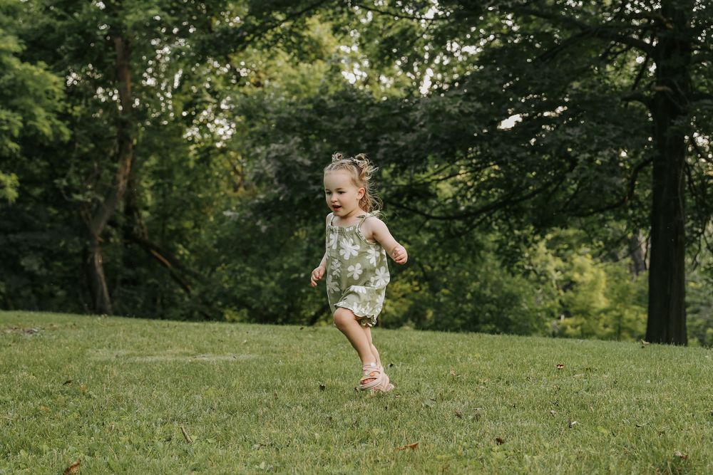 Young child runs carefree across a grassy hillside in a floral dress on a summer afternoon.