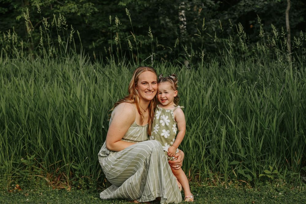 Two people in coordinating white outfits sitting together in front of tall grass during a summer photoshoot.