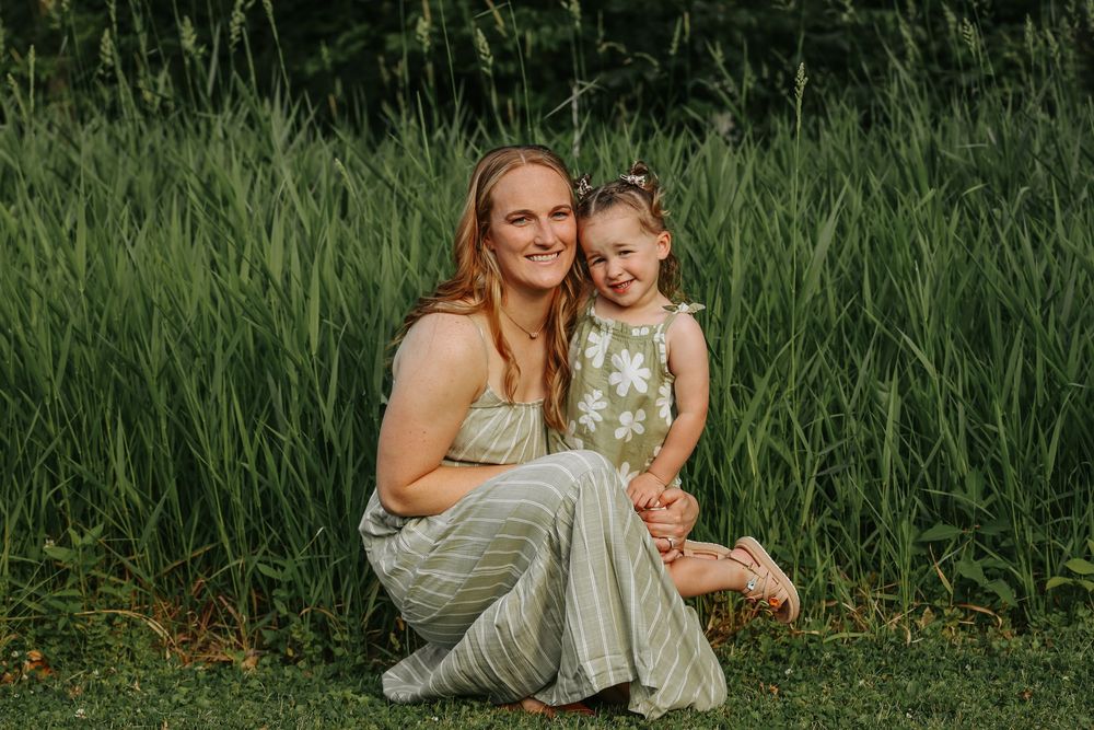 A couple embraces in a sunlit meadow surrounded by tall green grass and wildflowers.