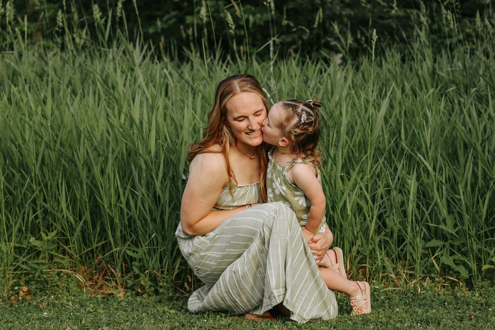 A tender moment captured between parent and child sitting together in tall green grass on a summer day.