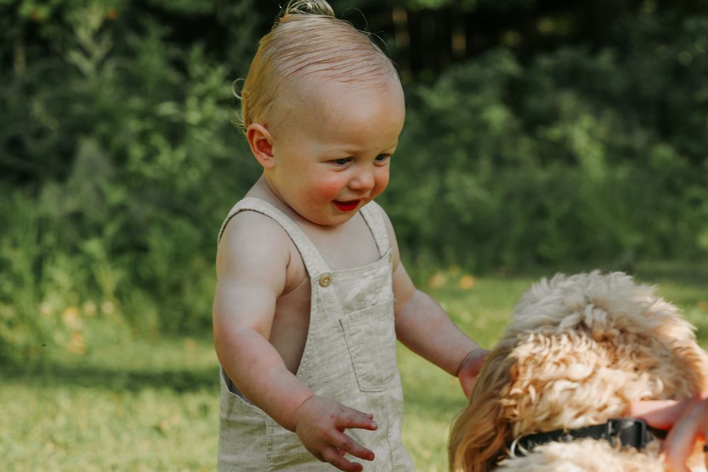 Young child in sleeveless outfit smiles with joy while playing outdoors in sunny garden setting.
