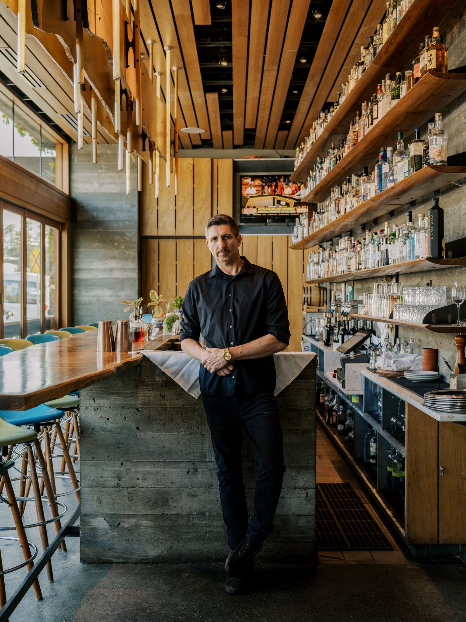 Modern bar interior with wooden shelving displaying liquor bottles and industrial concrete design elements.