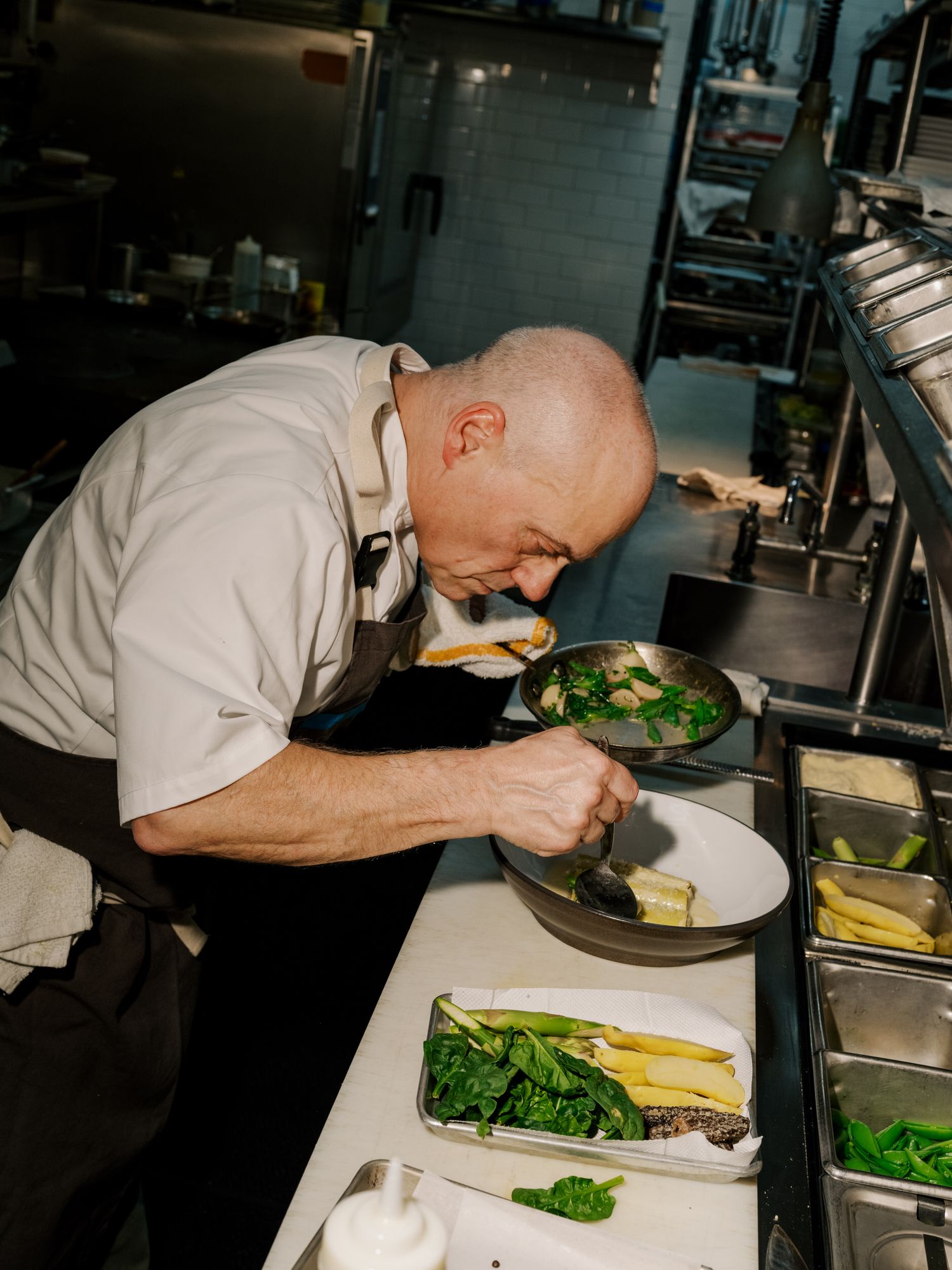 Chef working in professional kitchen carefully prepares fresh vegetables on wooden cutting board.
