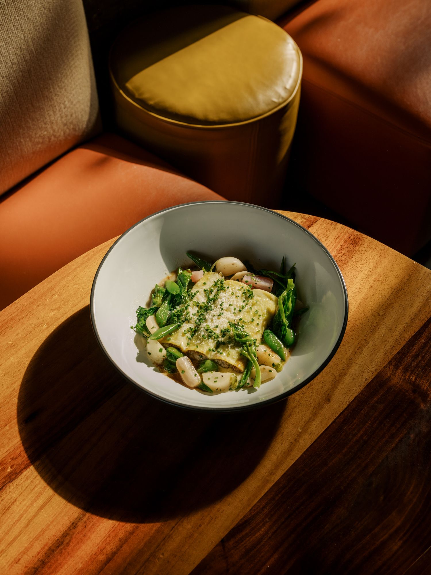 A bowl of creamy gnocchi pasta with fresh herbs and greens is artfully presented on a wooden surface.