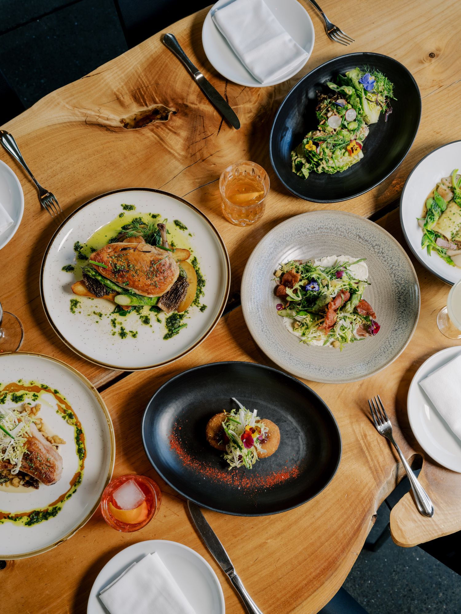 Elegant plated dishes and beverages arranged on a wooden table at an upscale restaurant showing multiple dining courses.