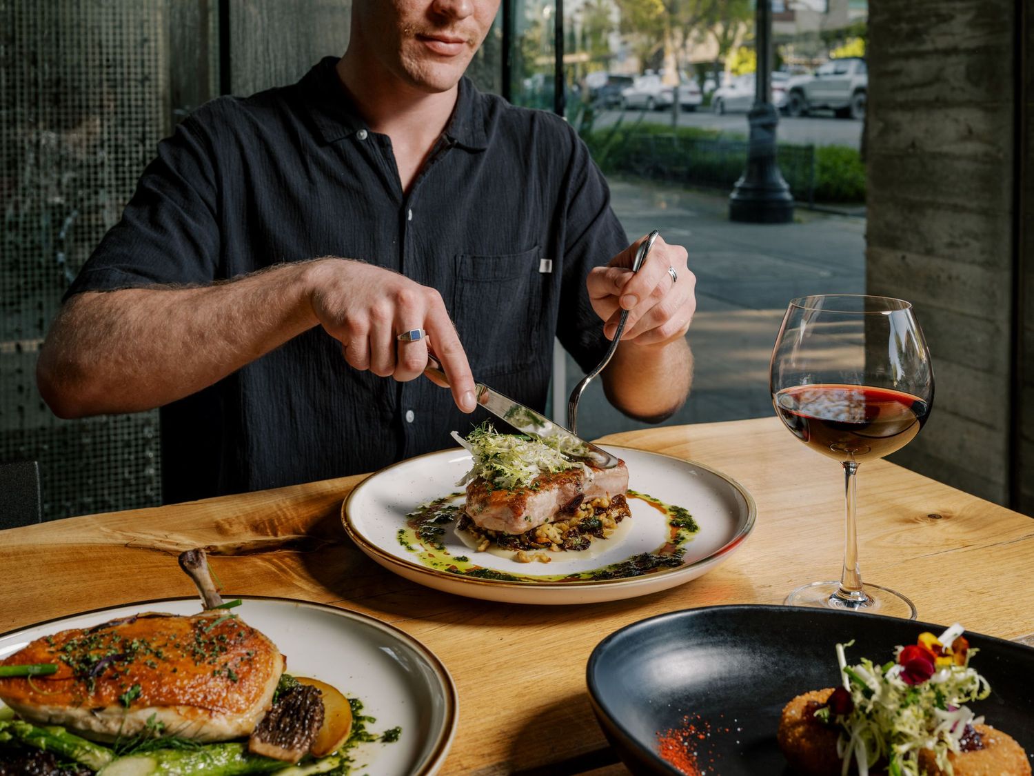 Person enjoying a fine dining experience with multiple plated dishes and red wine at an outdoor restaurant table.