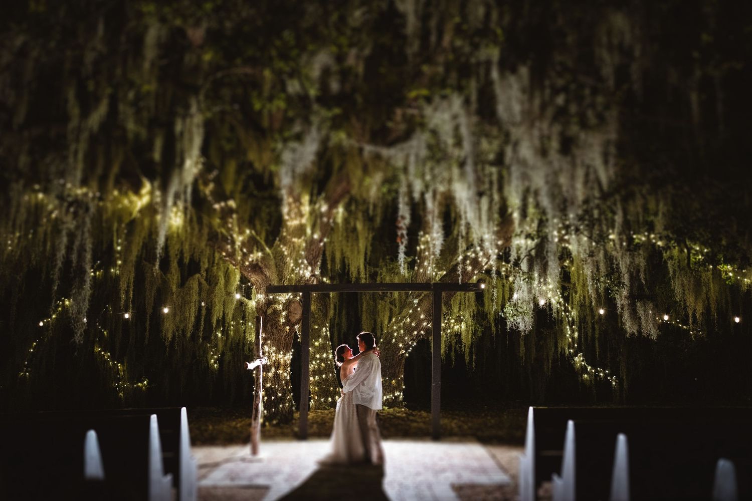 A dreamy outdoor wedding ceremony setup with hanging Spanish moss and glowing candles creating a mystical atmosphere.