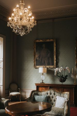 Elegant vintage room with crystal chandelier, antique furniture, and green wallpapered walls featuring a gilded portrait frame at Rise Hall.