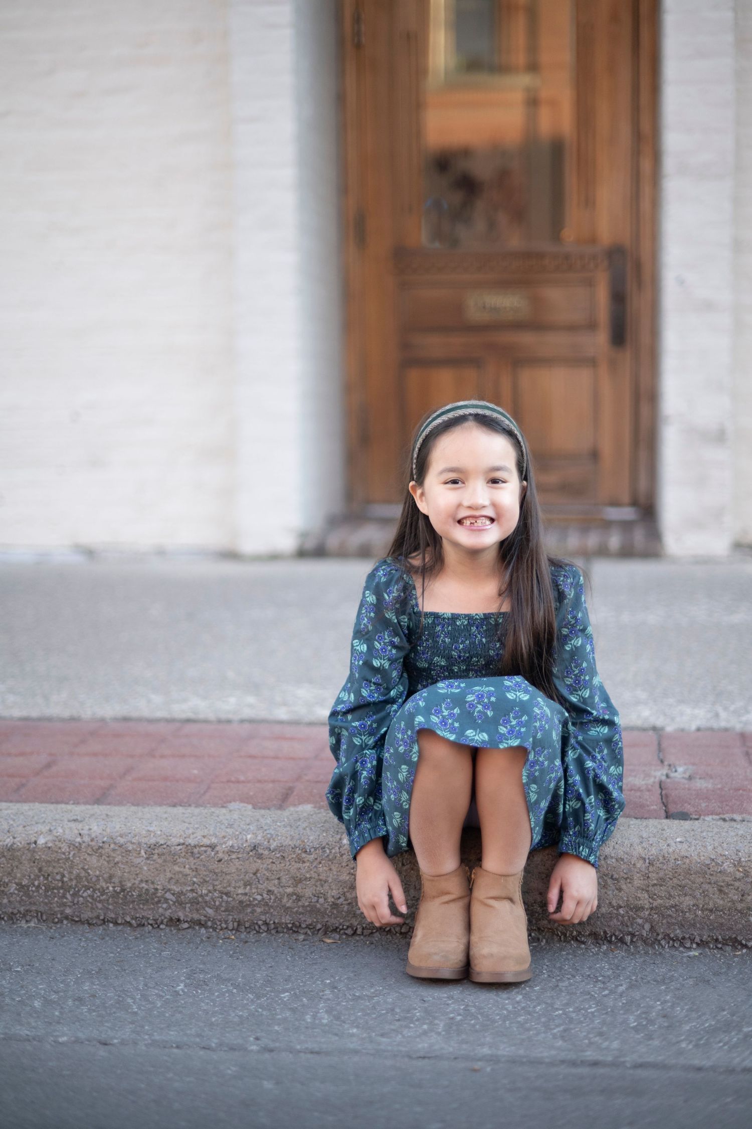 Young person in blue dress and boots sitting on steps in front of wooden door in downtown Franklin