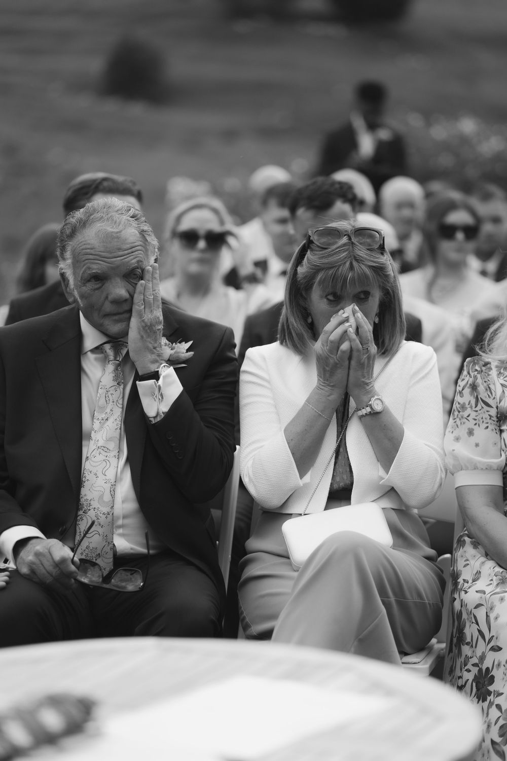 Emotional wedding guests wipe away tears during a touching ceremony moment in black and white photography.